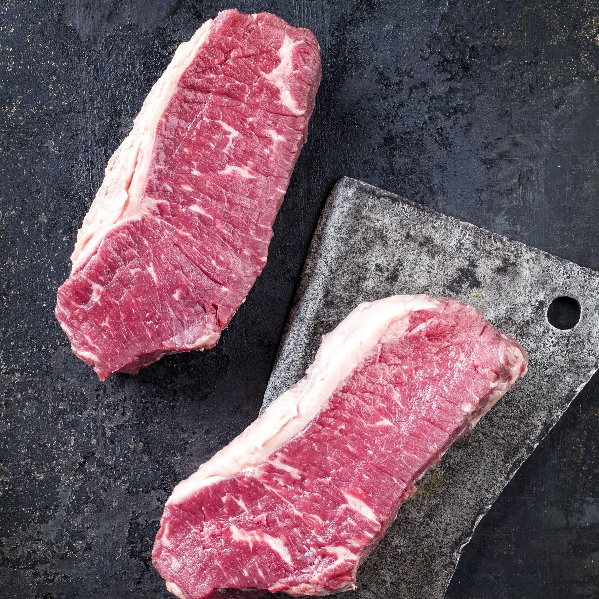 Raw cuts of marbled beef steak on a dark surface, showcasing their rich red color and texture, ideal for grilling or roasting.